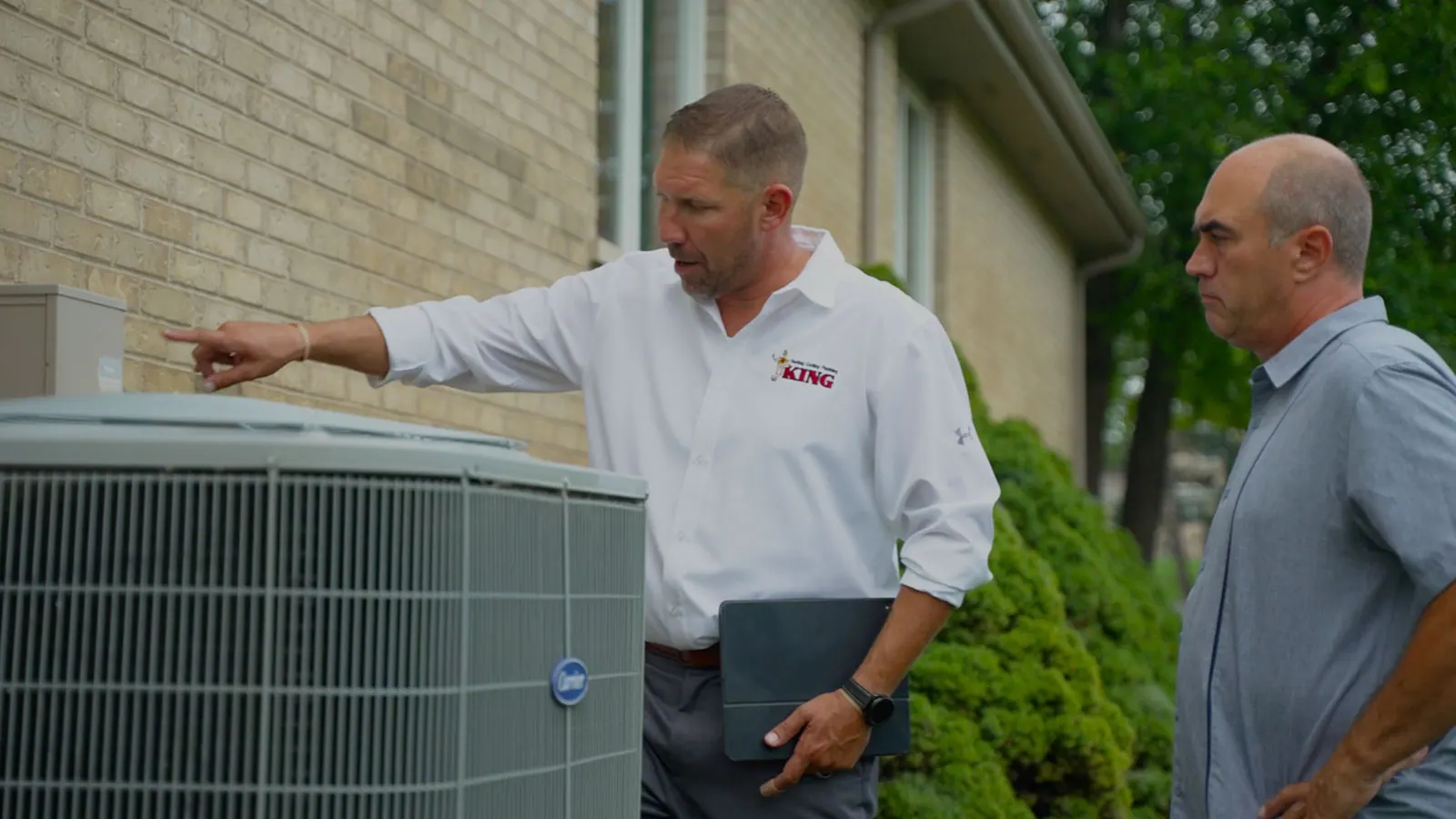 A King technician in a white shirt inspecting an AC unit with a homeowner