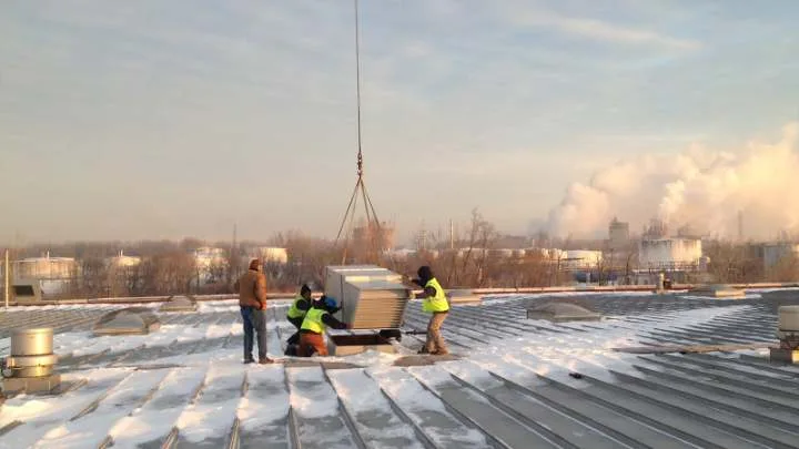 A helicopter lifting a rooftop HVAC unit onto a commercial building