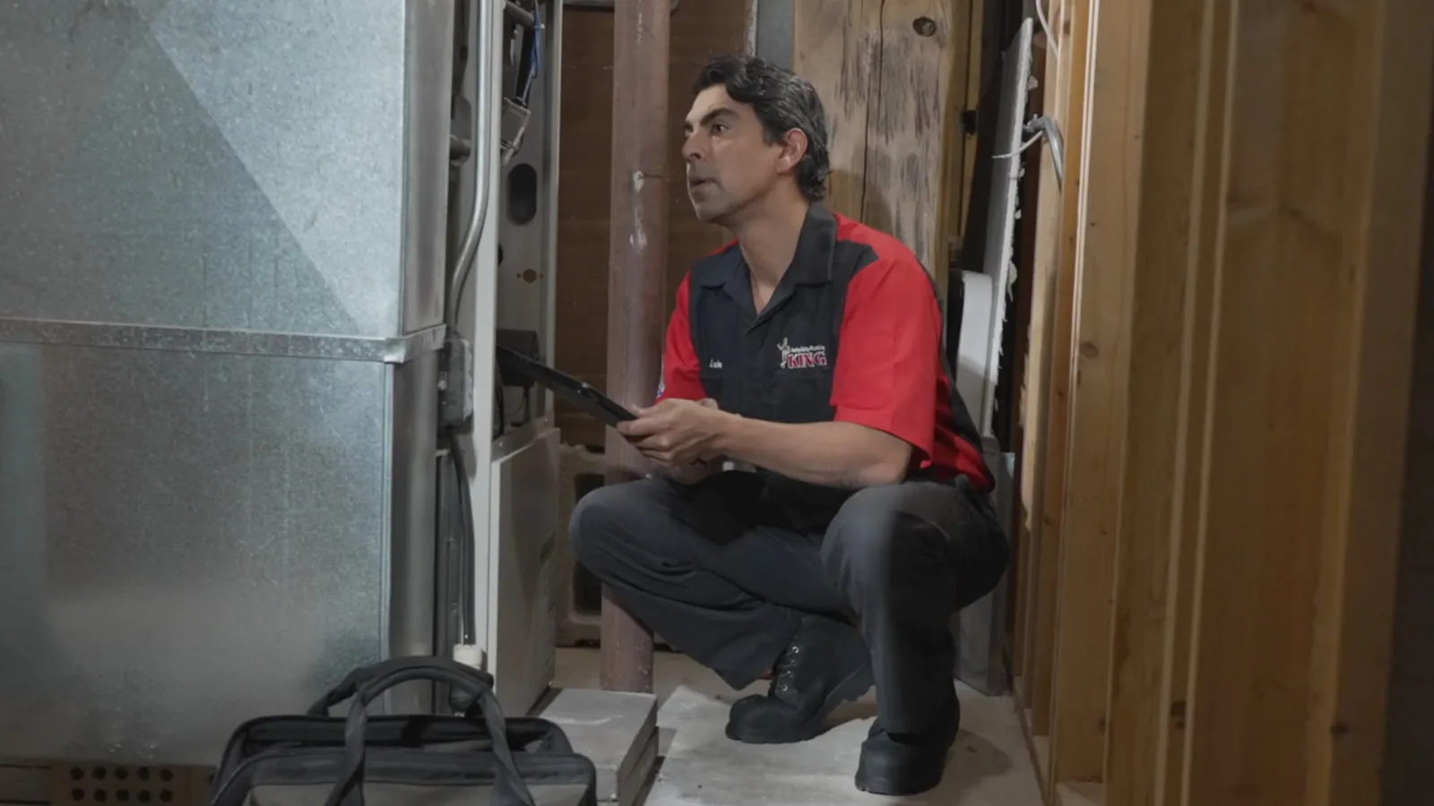 A King technician kneeling by a furnace with a tablet