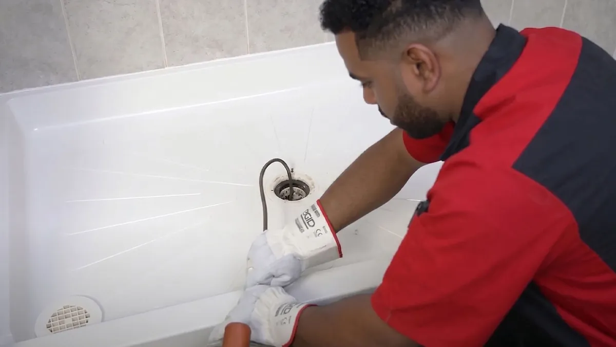 A King plumber running a drain cable into a shower drain