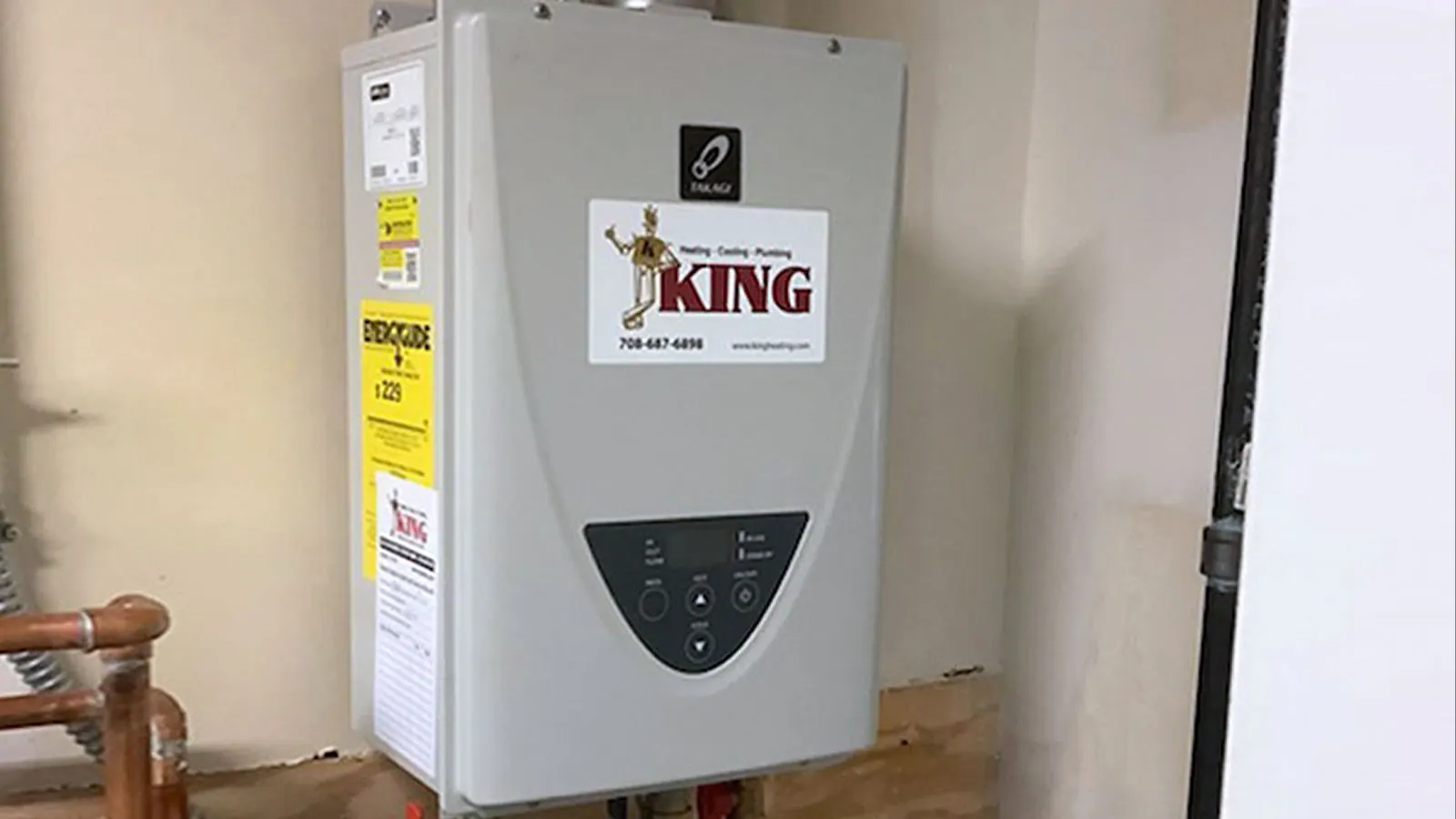 A tankless water heater with a King sticker mounted on a basement wall