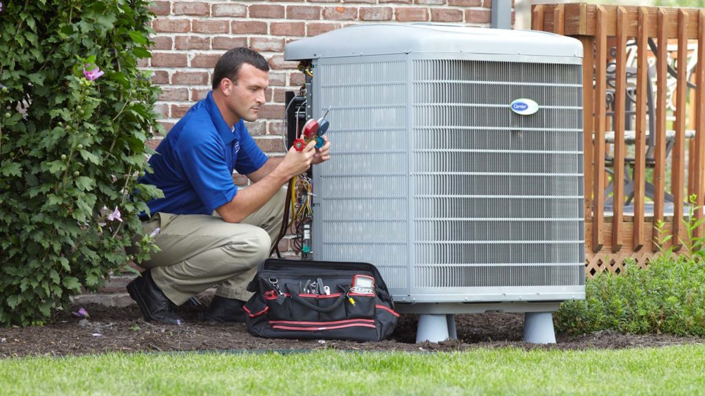 A King technician kneels next to a newly installed Carrier air conditioning system, checking its refrigerant levels.