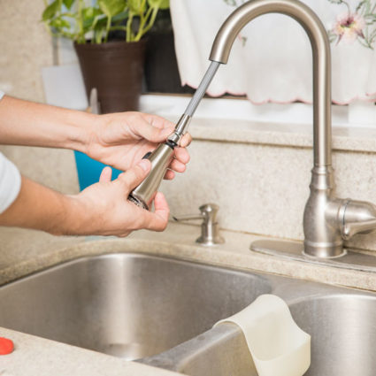 A King plumber attaches a spray nozzle to a kitchen sink spout as part our plumbing installation service.