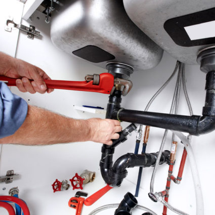 After replacing a section of pipe, our plumber uses a large wrench to attach a drain pipe underneath a home's kitchen sink.
