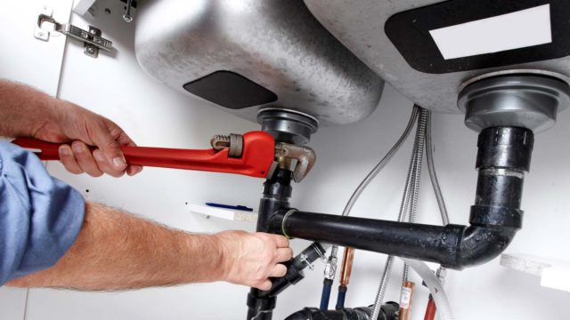 After replacing a section of pipe, our plumber uses a large wrench to attach a drain pipe underneath a home's kitchen sink.